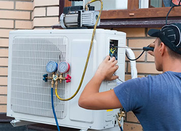 HVAC technician checking an outdoor air conditioner with refrigerant gauges during AC maintenance in Shanty Bay