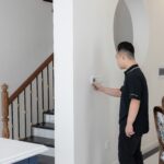 Man adjusting a wall thermostat in a hallway beside a staircase inside a house